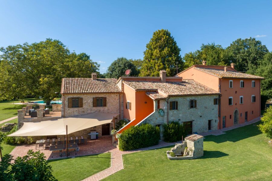 Charming Italian villa with stone facade, ochre stucco, terracotta roofs, and lush surroundings.