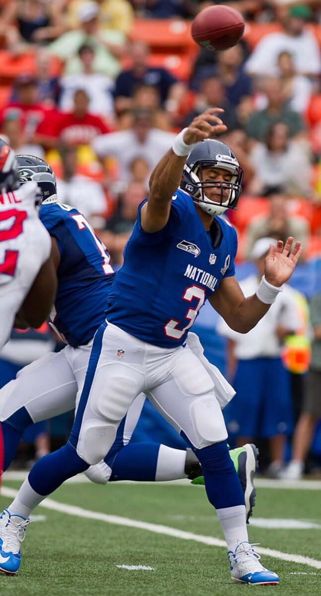 Russell Wilson, NFL quarterback, stands ready to make a play on the football field, wearing his team uniform