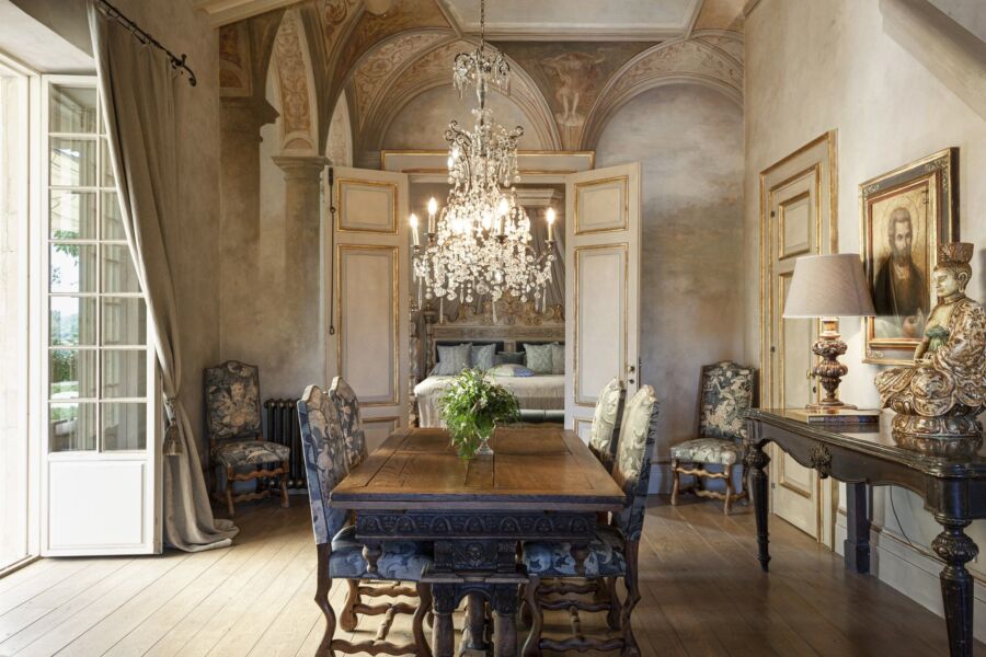 Elegant dining room with rustic table, chandelier, plush chairs, and cozy sleeping nook.