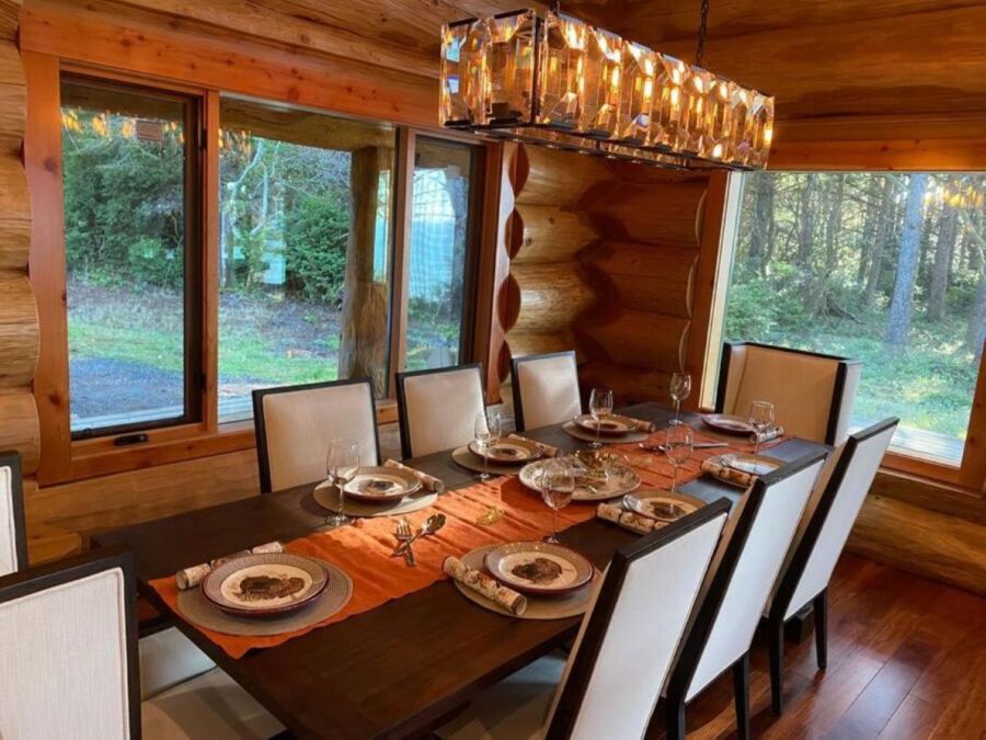 Rustic dining room with log walls, large windows, and modern chandelier.