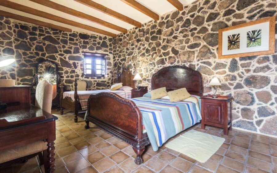 Rustic stone bedroom with wooden beams, terracotta floor, traditional beds and cozy rural hotel decor.