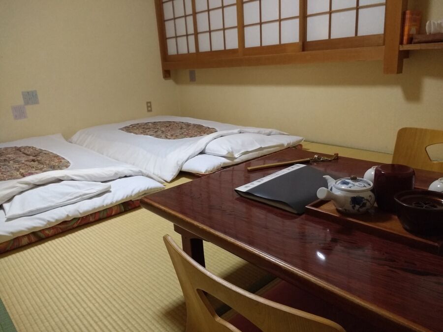Interior of Ryokan Matsumae Nara showing a cozy room with two beds and a table, ideal for guests.
