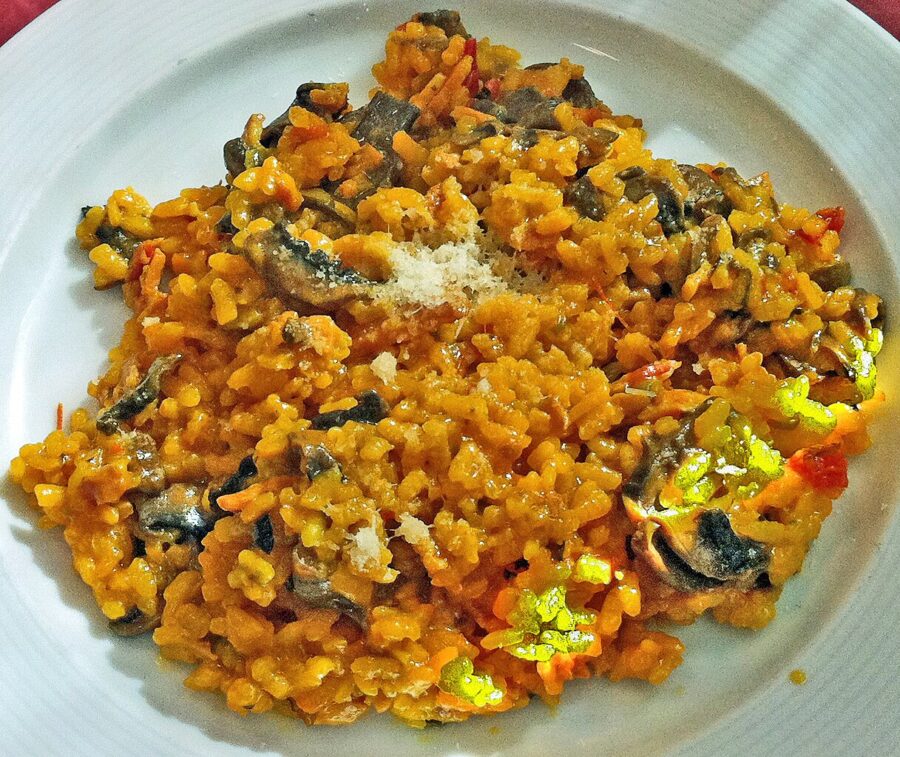 Saffron risotto with mushrooms, diced vegetables, and cheese on a white plate.