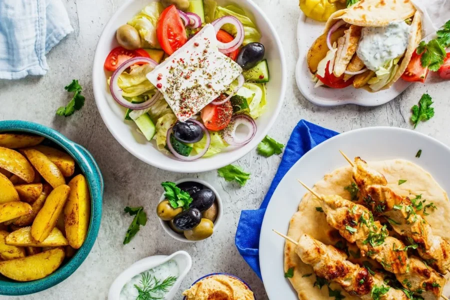 Mediterranean feast: Greek salad, potato wedges, chicken skewers, and olives.