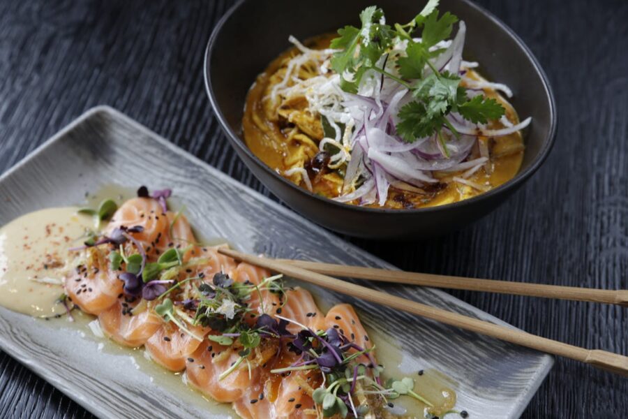 Modern cuisine: salmon sashimi and noodle dish with vibrant garnishes on a textured black surface.