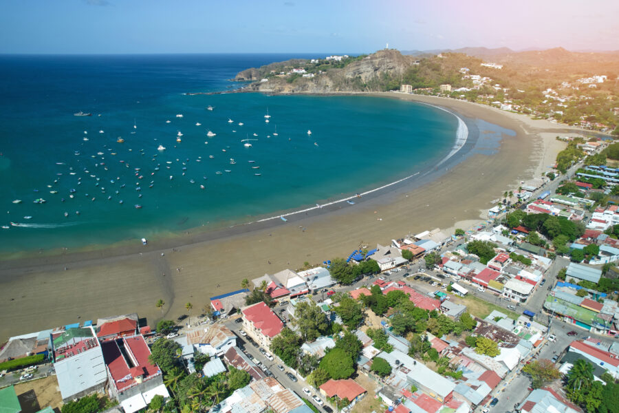 Panoramic aerial shot of San Juan del Sur Beach, featuring vibrant blue waves, sandy shores, and surrounding greenery