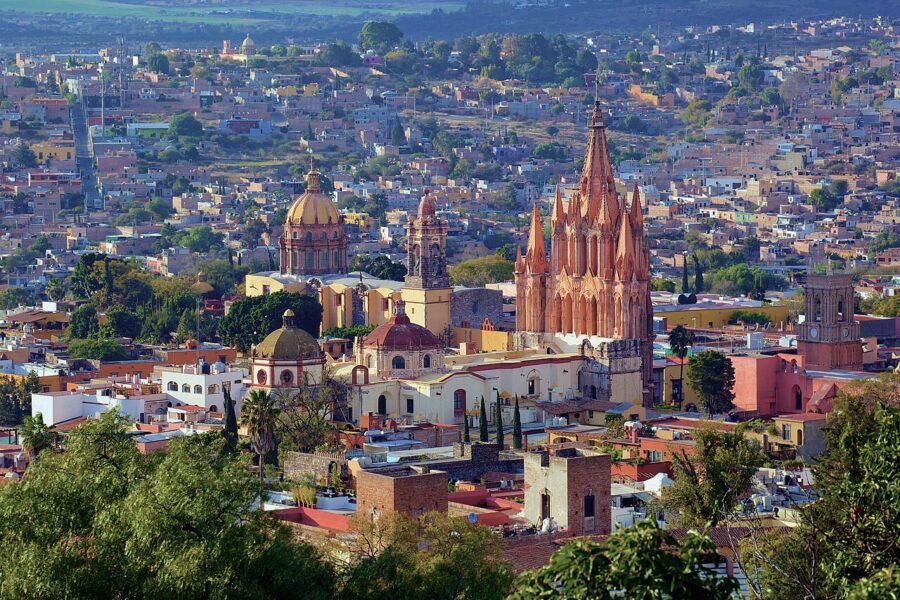 Panoramic view of San Miguel de Allende featuring numerous buildings and lush trees under a clear sky.