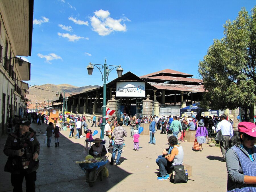 People walking through the lively San Pedro Market plaza in Cusco, Peru, engaging with vendors and exploring the area.