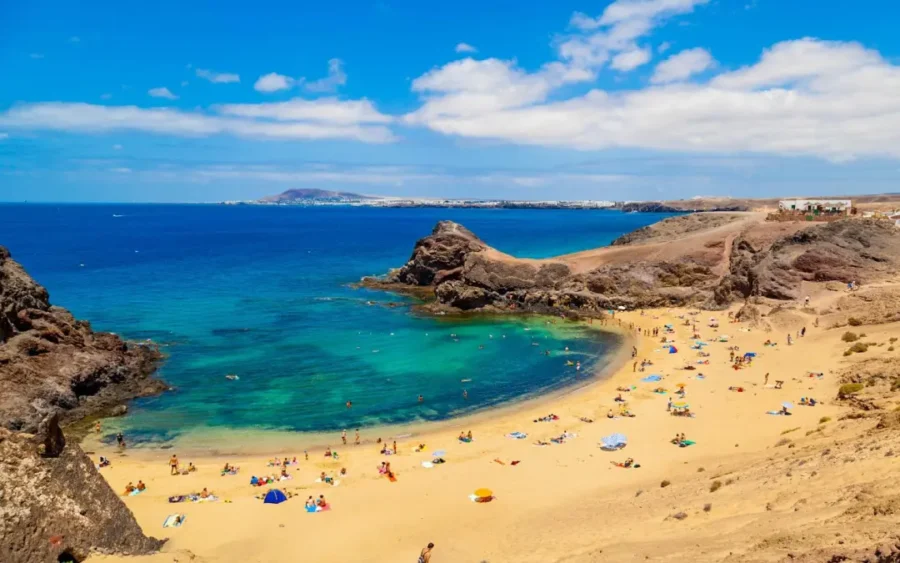 Lanzarote Canary Islands crescent sandy beach cove with turquoise water and volcanic cliffs.