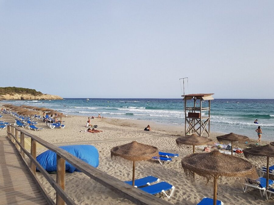 Santo Tomas beach in Menorca, showcasing vibrant umbrellas and beach chairs set up on the golden sand.