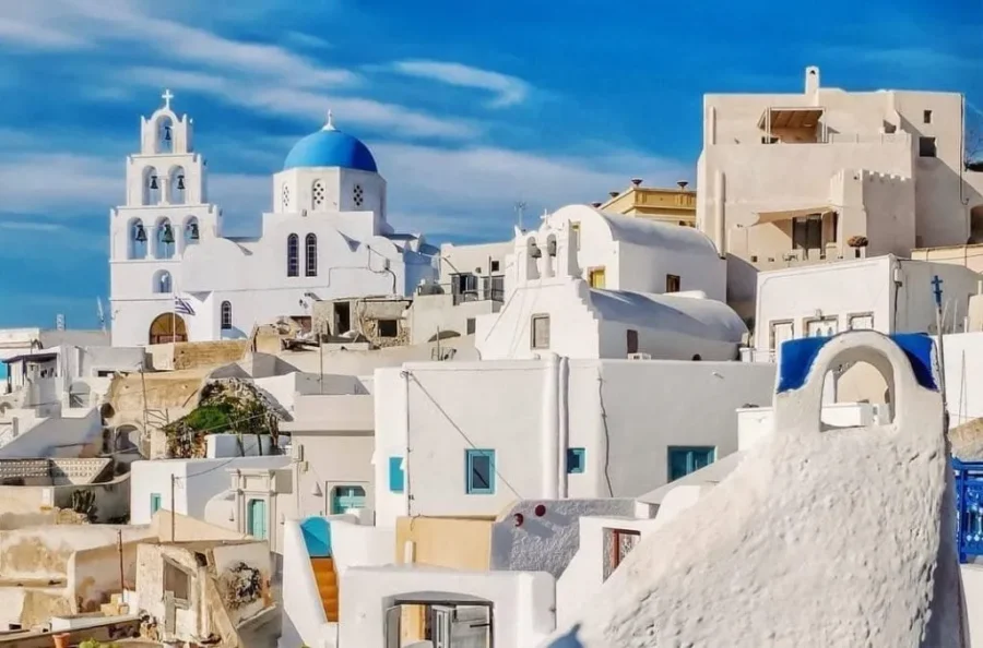 Santorinis iconic white buildings and blue domes in Pyrgos under a bright sky.