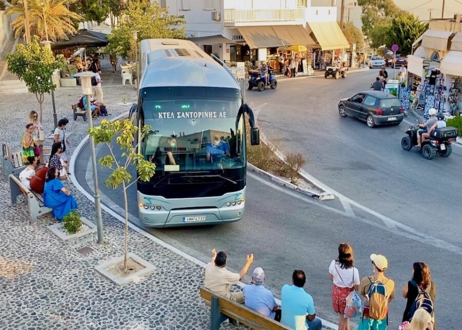 Santorini street scene with tourists, locals, and bus reflecting vibrant Mediterranean culture.
