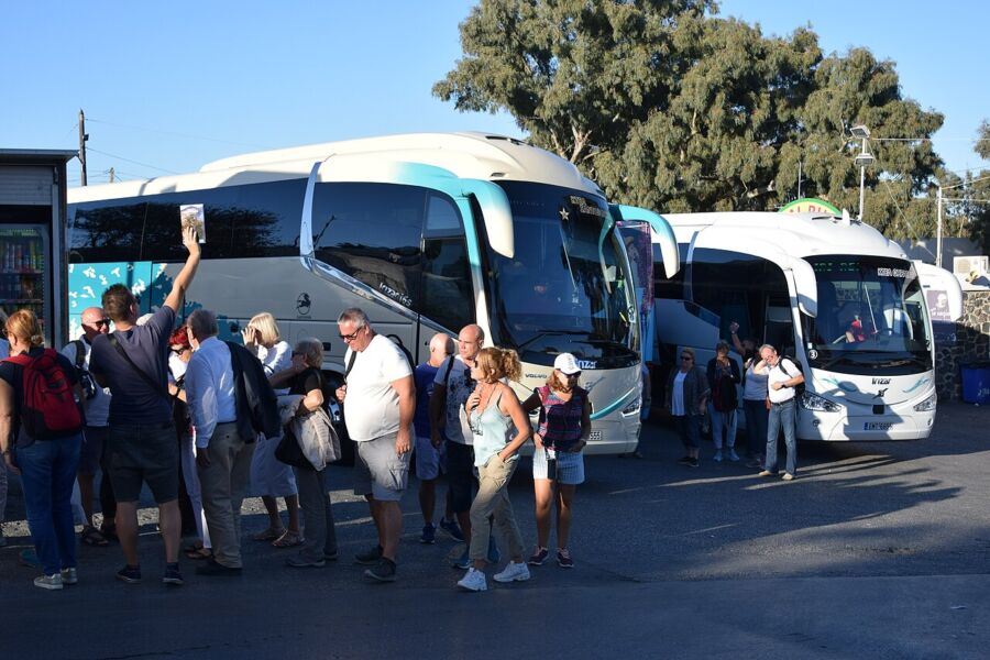 Tourists boarding buses in Santorini, surrounded by scenic views of the island's iconic architecture and vibrant atmosphere.