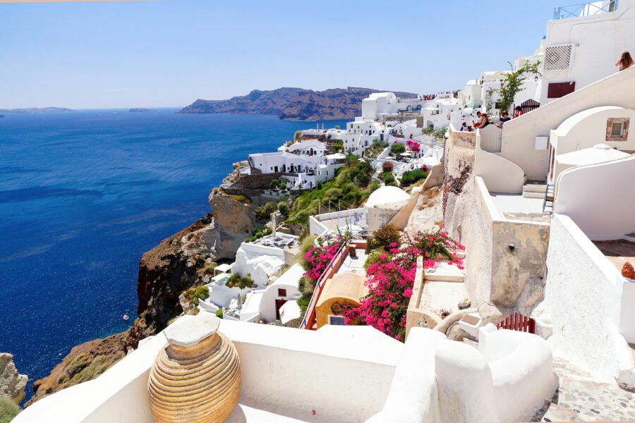 Santorini cliff view with iconic whitewashed buildings, Aegean Sea, and vibrant bougainvillea.