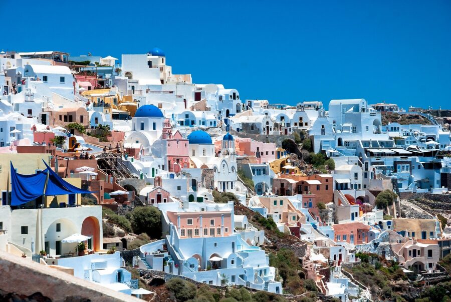 Santorini cliffside view with iconic white-washed Cycladic architecture and blue domes against the Aegean Sea.