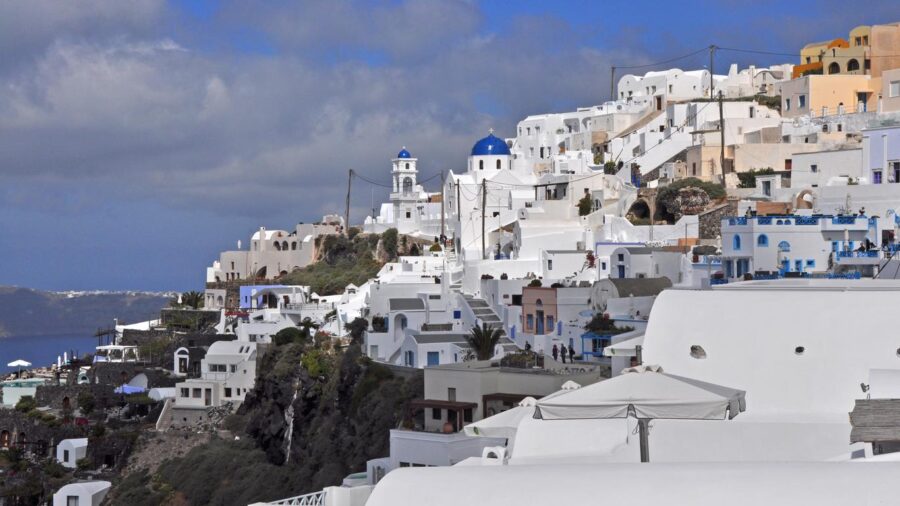 Scenic Santorini village with white architecture, blue domes, sea view, and lush greenery.