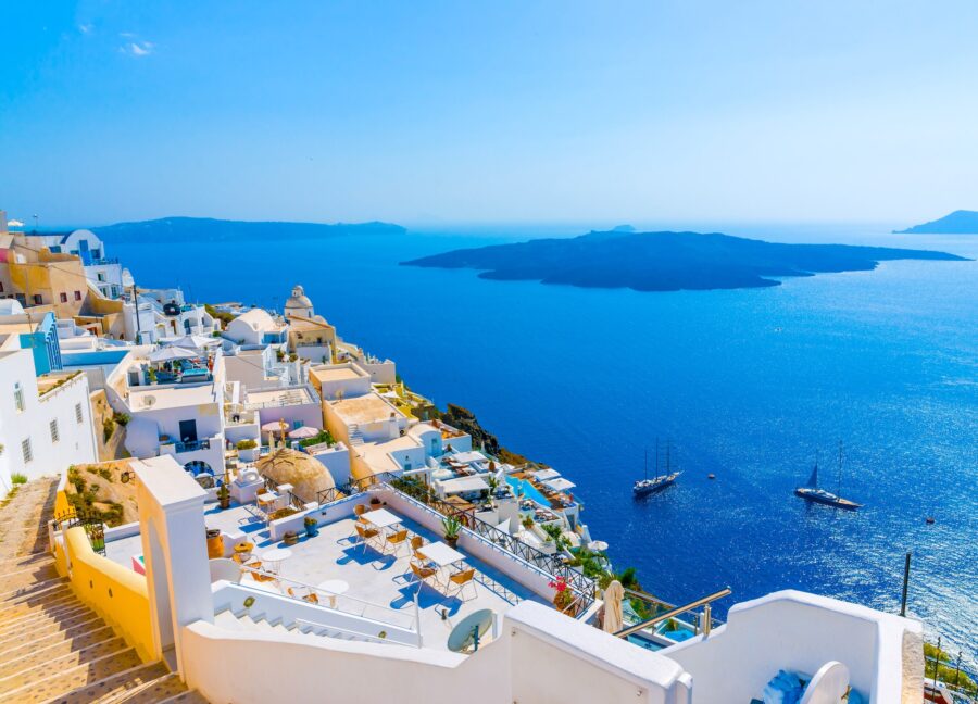 Santorini coastal town with white-washed architecture, blue accents, Aegean Sea views, and boats.