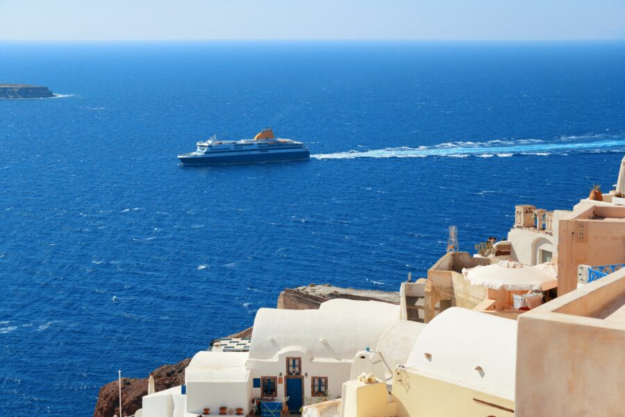 Ferry ship navigates towards Santorini island, with its famous whitewashed buildings and cliffs visible against the sea