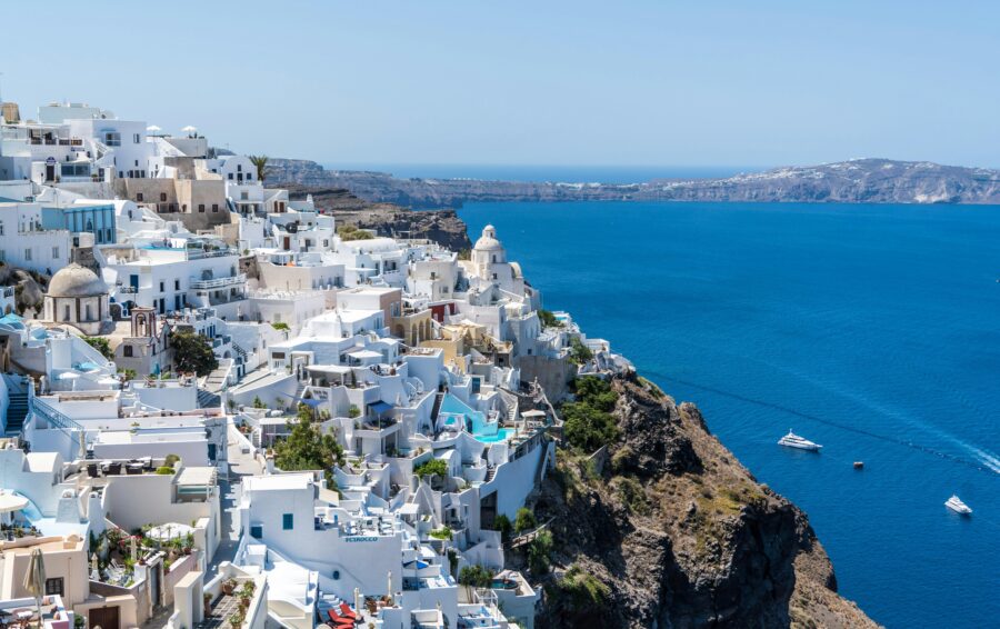 Santorini Greece coastal view with white-washed buildings, blue sea, clear sky, and boats.