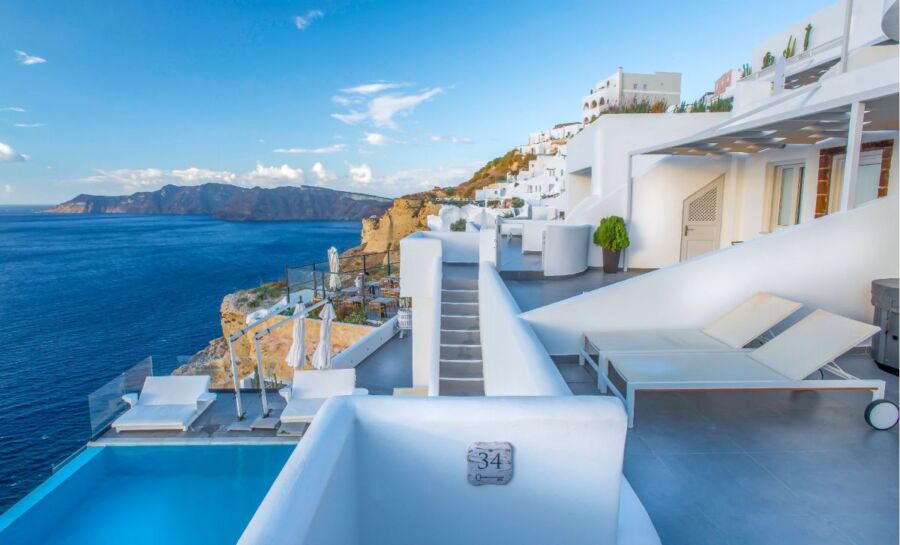 Luxury Santorini villa on cliff, whitewashed walls, ocean view, Mediterranean architecture.