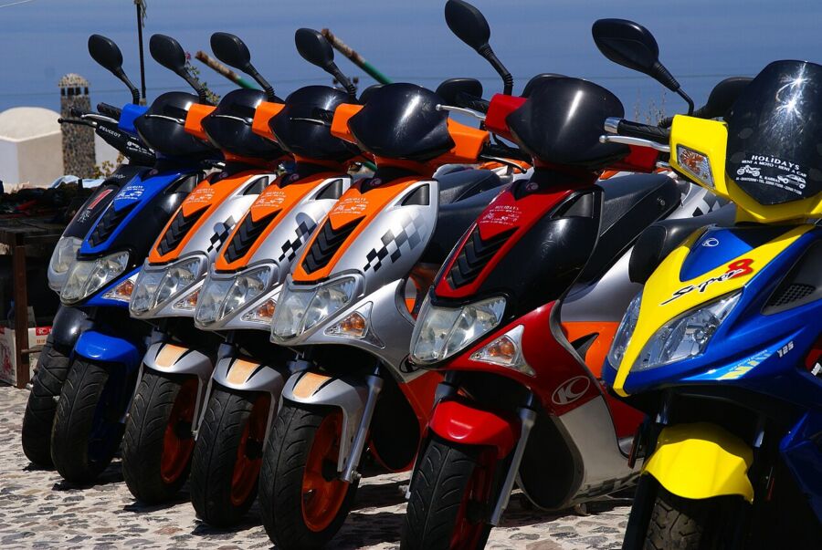 Multiple scooters lined up in Santorini, highlighting their sleek designs and vibrant colors.