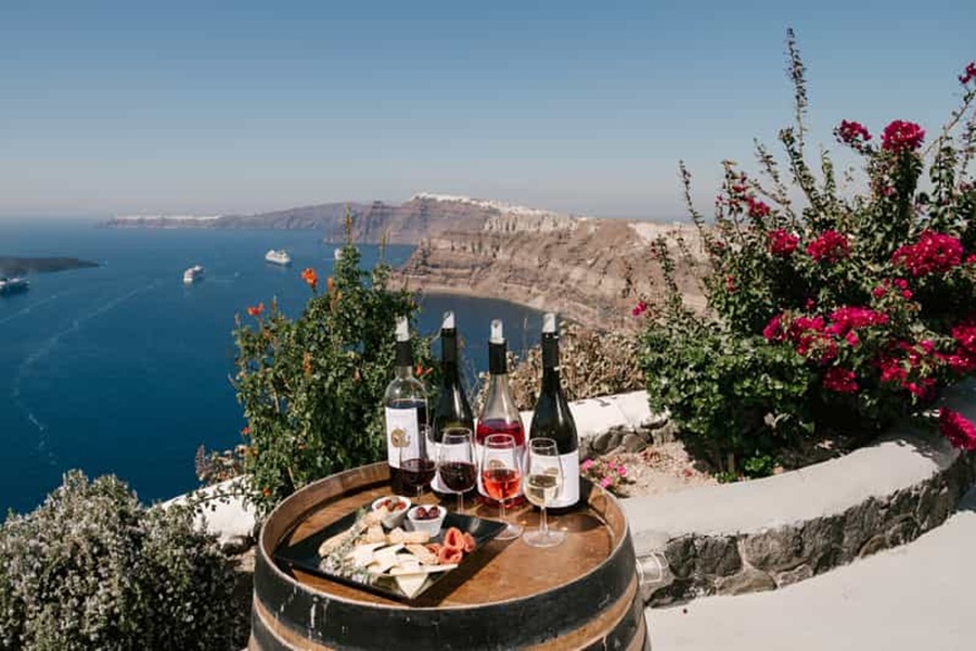 Wine and cheese by Aegean Sea with Santorini cliffs and blooming bougainvillea.
