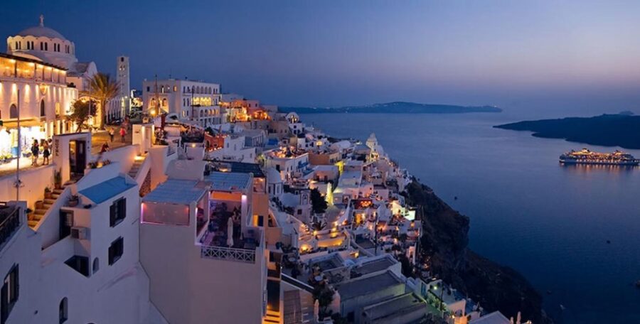 Twilight scene of Santorinis coastal town with whitewashed buildings, blue domes, and serene water.