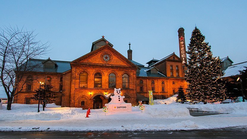 Sapporo Beer Museum historic red-brick brewery in winter snow at night with lights and decorations.