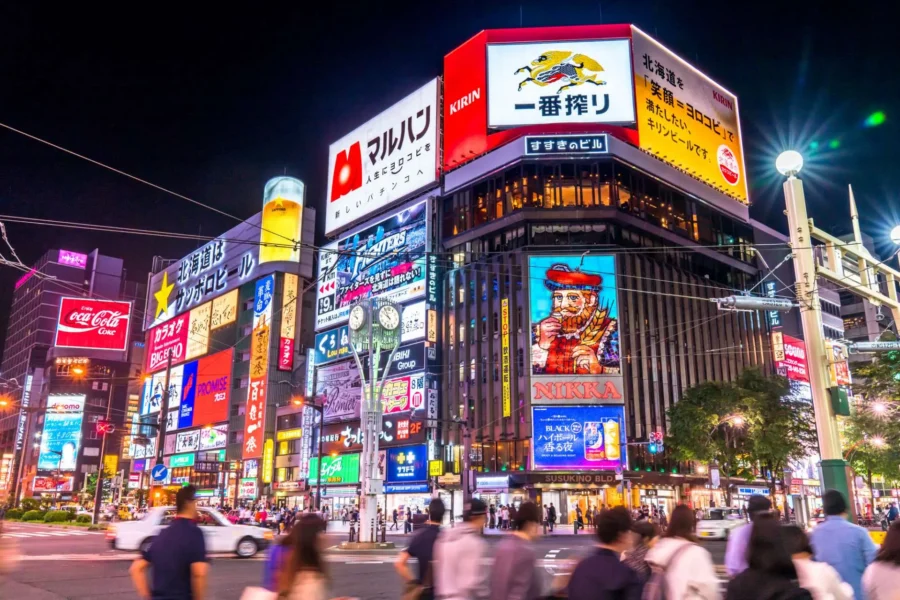 Sapporo Susukino nightlife district with neon signs, billboards, and pedestrians at a busy crosswalk.