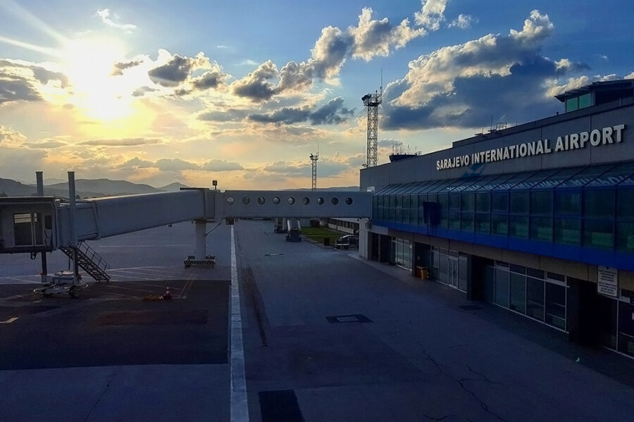 Sarajevo International Airport at sunset, showcasing modern architecture amid a serene mountainous backdrop.