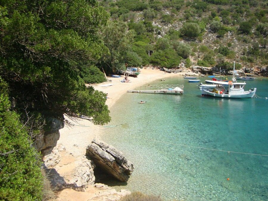 Sarakiniko Beach in Greece, showcasing boats on the water and visitors relaxing on the sandy shore.
