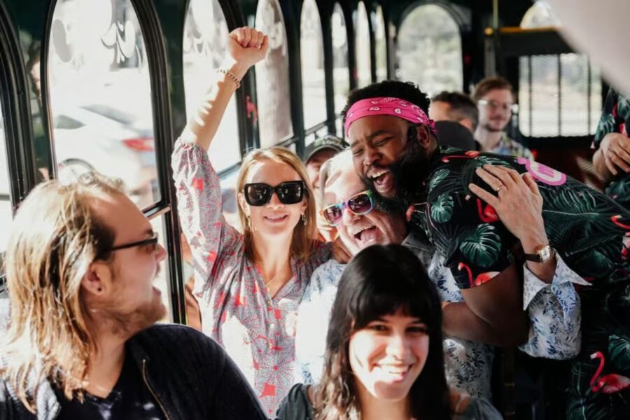 Inside a bus, a group of people gathers as one person raises a sign for the "Savannah For Morons Guided Comedy Tour."