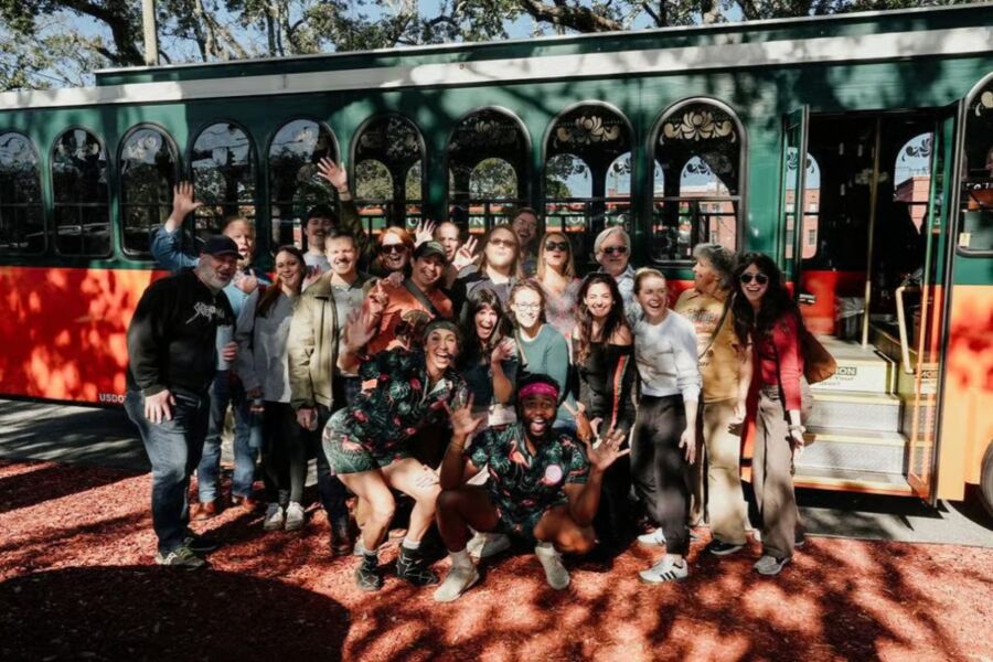 Tour participants pose cheerfully in front of a trolley, celebrating their experience on the Savannah For Morons Guided Comedy Tour.