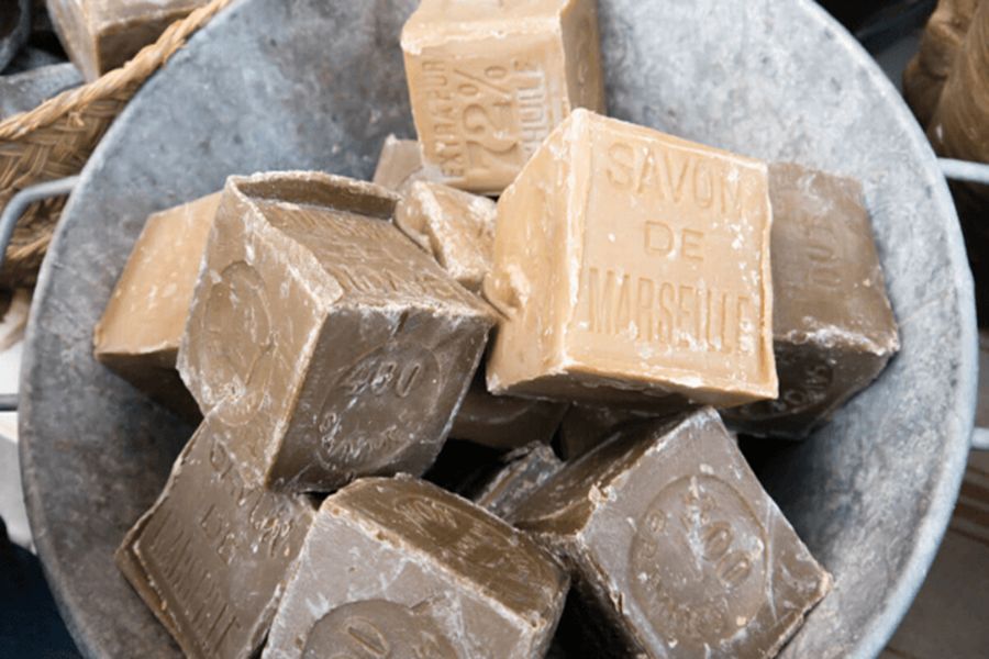 Marseille soap cubes in rustic metal bucket, traditional craftsmanship display, earthy tones, embossed markings.