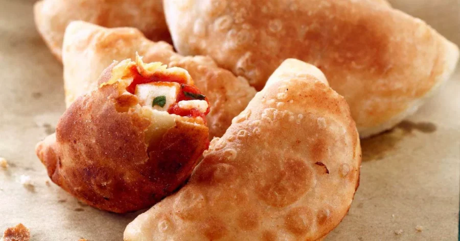 Golden brown panzerotti with colorful filling on parchment background. Delicious homemade appearance.