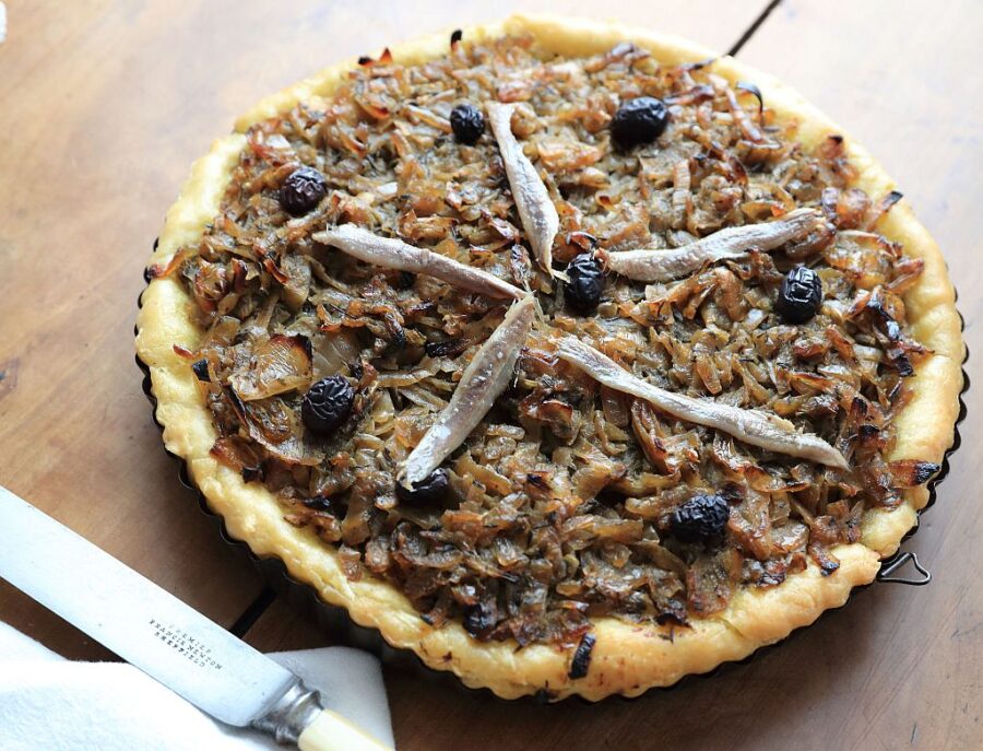 Golden crust Cannes Pissaladière with caramelized onions, olives, and anchovies on rustic table.