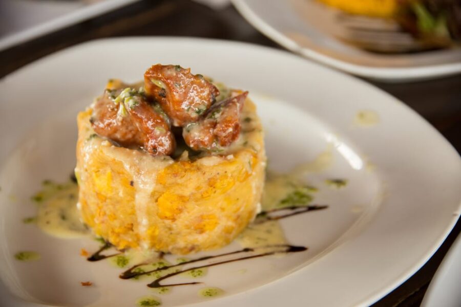 Gourmet mofongo with creamy sauced pork on mashed plantains, plated with artistic sauces.