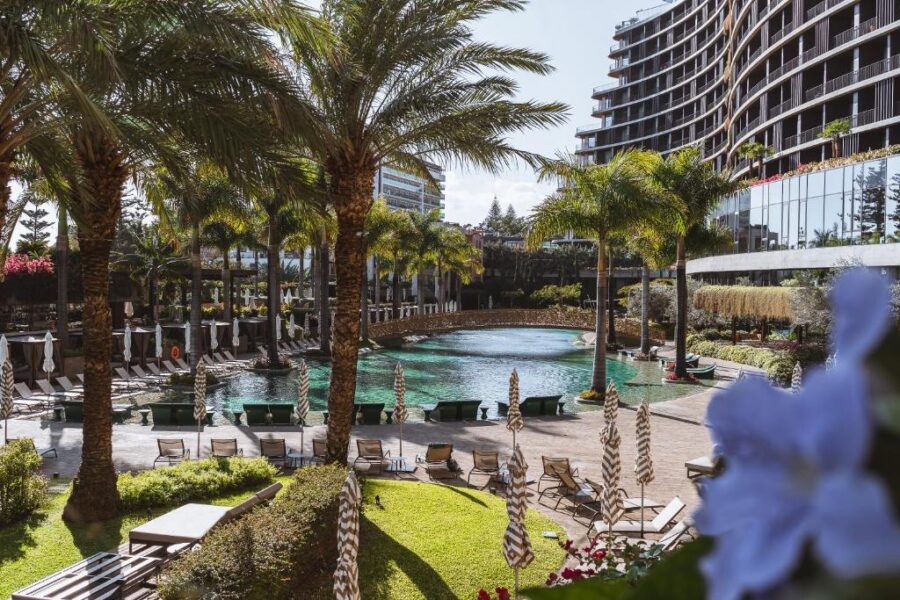 Scenic view of the pool and palm trees at Savoy Palace hotel in Madeira, highlighting a relaxing vacation setting.
