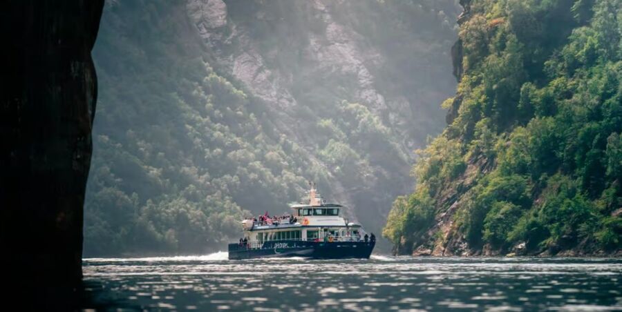 Scenic ferry journey through lush, towering cliffs with passengers enjoying tranquil views.