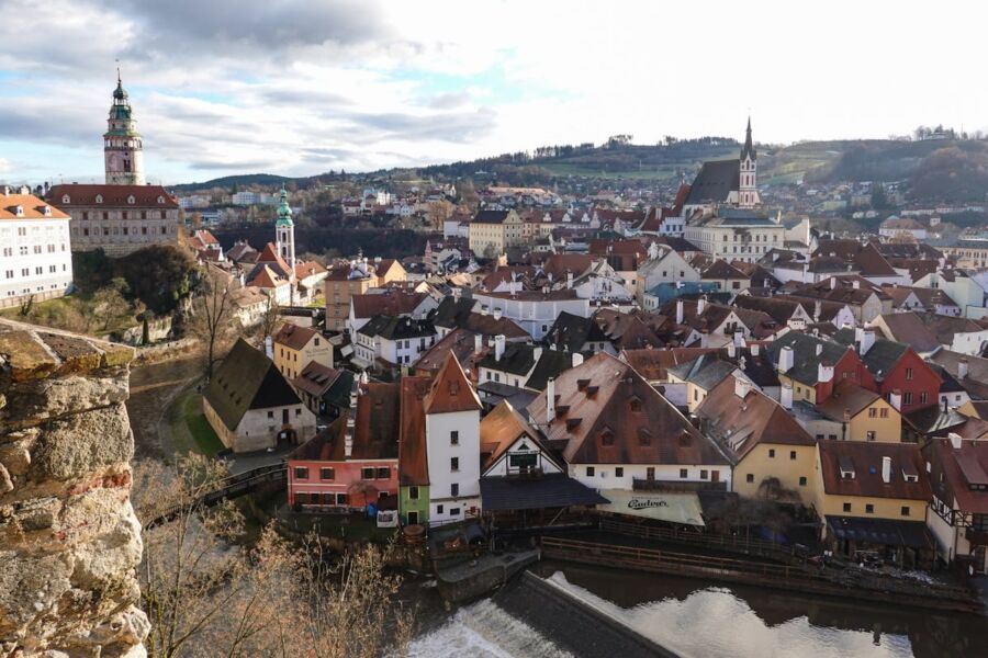 Panoramic view of a charming medieval town with a castle, colorful rooftops, and a serene waterway.
