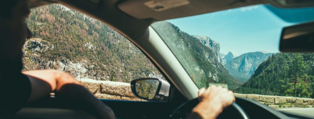 Scenic mountain drive: car interior steering wheel overlooking pine-filled valley and rocky cliffs.