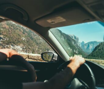 Scenic mountain drive: car interior steering wheel overlooking pine-filled valley and rocky cliffs.
