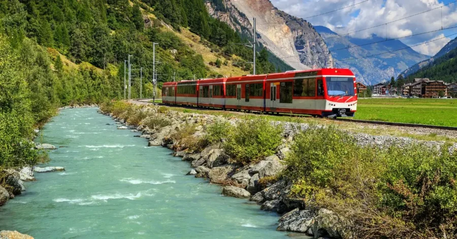 Scenic train through lush hills, turquoise river, and mountains; ideal Swiss travel landscape.