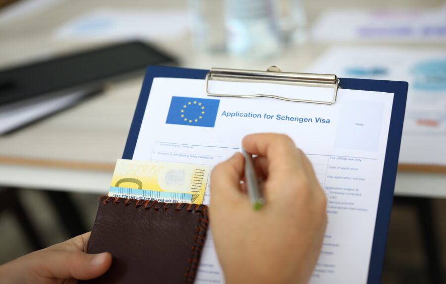 Hand of a man holding a folder with a passport and cash, engaged in answering Schengen visa application queries.