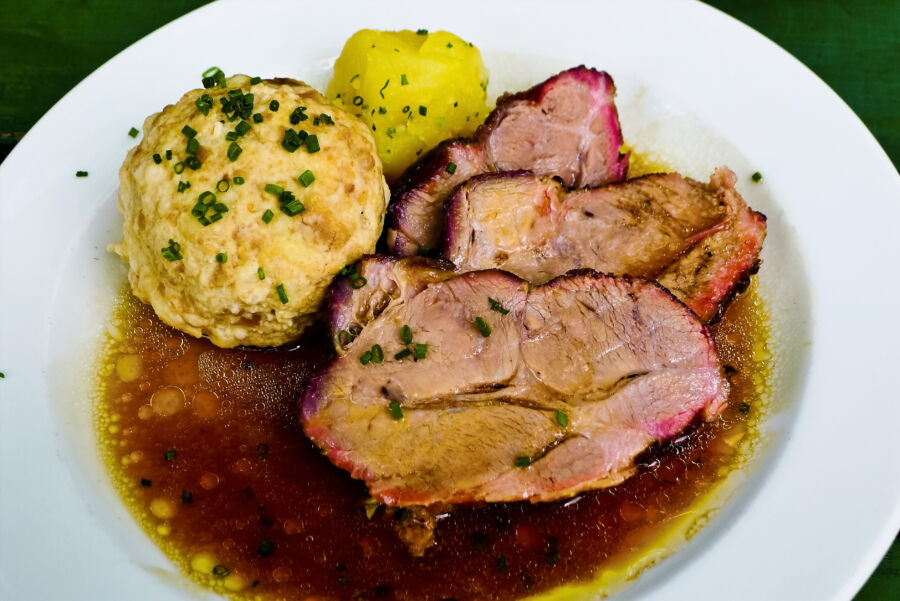 Roast pork (Schweinsbraten) served on a plate, garnished with herbs and accompanied by side dishes