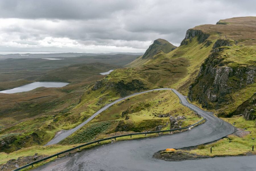 Winding mountain road in Scottish Highlands amidst rugged cliffs and ominous sky.