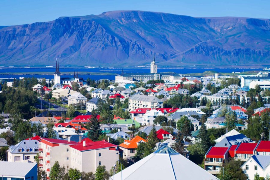 Aerial view of Reykjavik: colorful rooftops, mountains, church spires, and fjord reflections.
