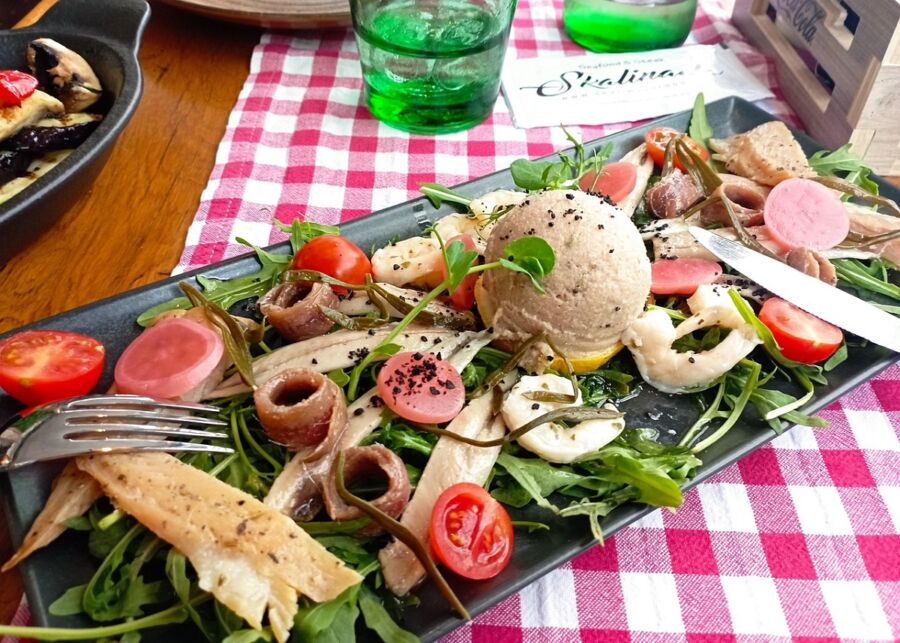 A vibrant seafood platter with arugula, tomatoes, pickled vegetables, and creamy seafood mousse.