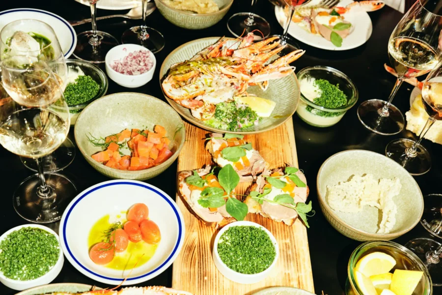 Seafood sharing board with prawns, crostini, condiments, and wine glasses.
