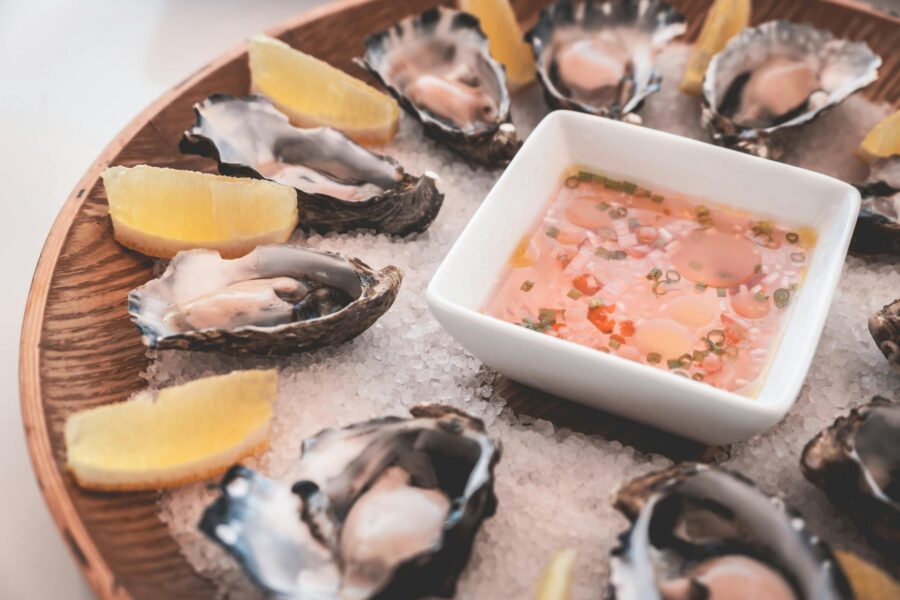 Platter of shucked oysters with lemon wedges and dipping sauce on coarse salt.